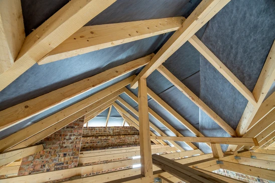Ouvrier en équipement de sécurité installant de l'isolation thermique entre chevrons de toiture dans combles en construction